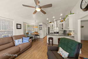 Living area featuring light wood-style flooring, a textured ceiling, vaulted ceiling, and a ceiling fan