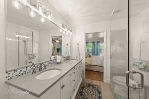 Ensuite bathroom featuring double vanity, light tile patterned floors, a textured ceiling, a shower stall, and a ceiling fan