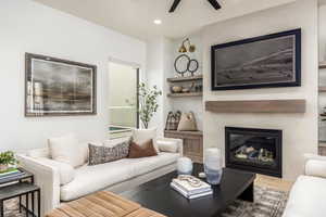 Living area with a glass covered fireplace, wood finished floors, recessed lighting, a ceiling fan, and built in shelves