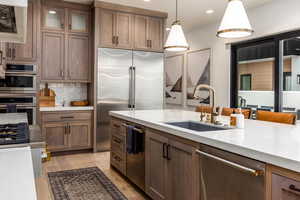 Kitchen with appliances with stainless steel finishes, light stone countertops, hanging light fixtures, brown cabinetry, and backsplash