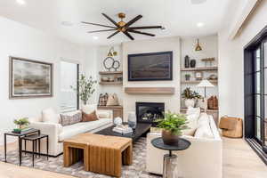 Living room featuring light wood-style floors, a fireplace, ceiling fan, recessed lighting, and built in shelves