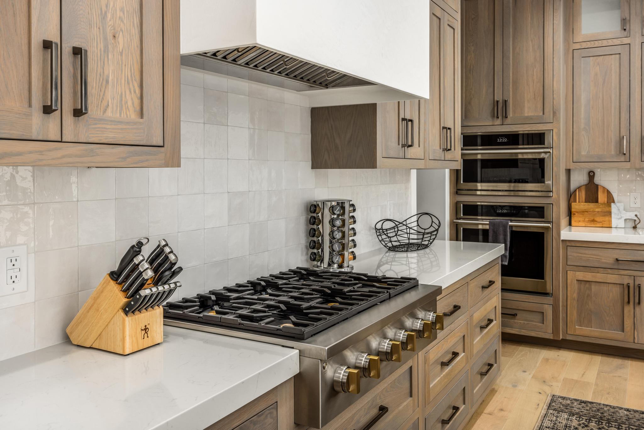 Kitchen featuring decorative backsplash, appliances with stainless steel finishes, custom exhaust hood, light stone countertops, and light wood-style floors