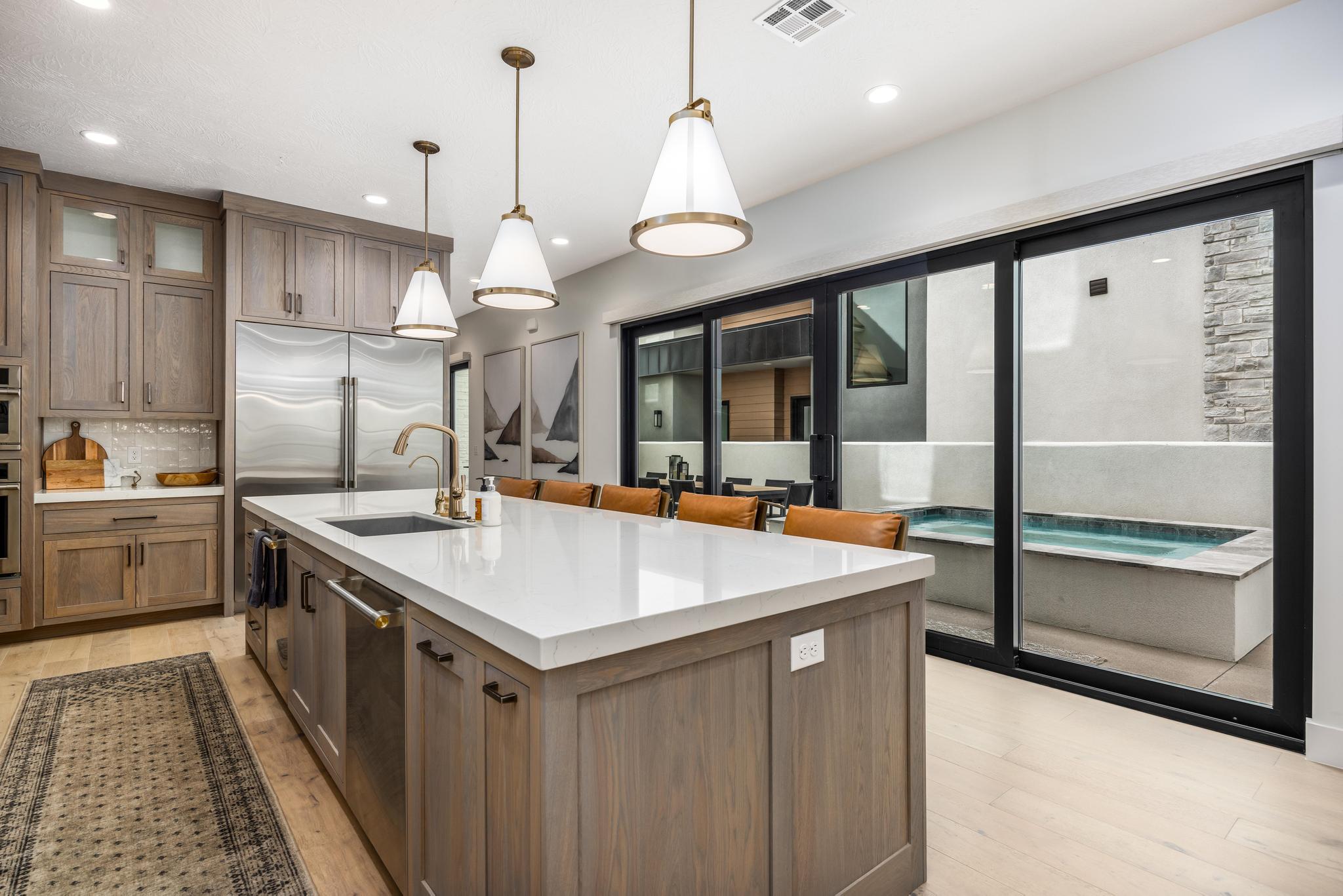 Kitchen featuring brown cabinets, hanging light fixtures, tasteful backsplash, an island with sink, and glass insert cabinets