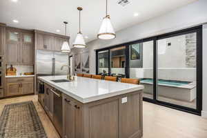 Kitchen featuring brown cabinets, hanging light fixtures, tasteful backsplash, an island with sink, and glass insert cabinets
