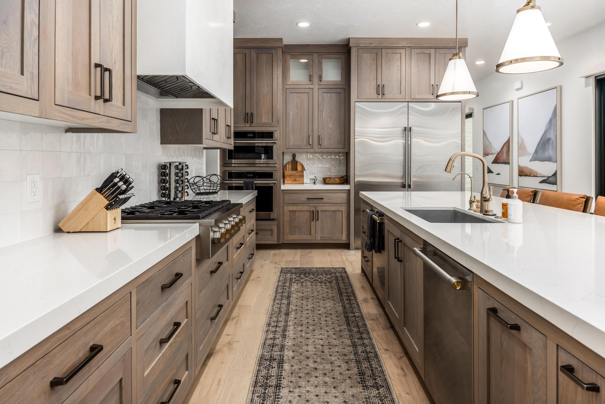 Kitchen featuring pendant lighting, custom exhaust hood, brown cabinetry, appliances with stainless steel finishes, and light stone counters