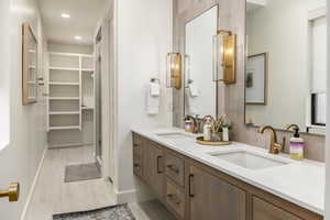 Full bath with double vanity, recessed lighting, a spacious closet, a stall shower, and light wood-style floors