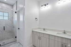 Bathroom with double vanity, light marble finish floors, and a marble finish shower