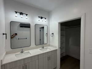 Full bath featuring double vanity, a spacious closet, and dark wood-type flooring
