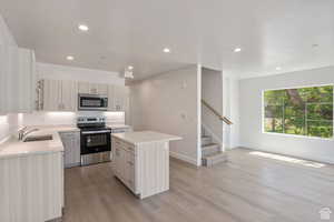 Kitchen featuring a center island, appliances with stainless steel finishes, recessed lighting, light wood-style floors, and light stone countertops