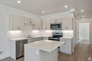 Kitchen with stainless steel appliances, light wood-type flooring, a center island, recessed lighting, and light stone counters