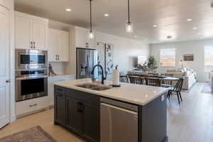 Kitchen with appliances with stainless steel finishes, open floor plan, white cabinetry, decorative light fixtures, and recessed lighting