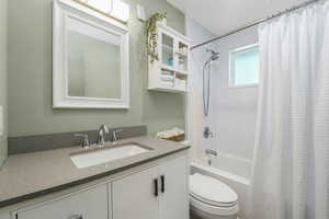 Main-floor full bath featuring updated tub/shower combination with curtain and updated vanity, and flooring.