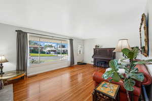 Living area featuring light hardwood flooring, pocket door to kitchen, and large window at the front.