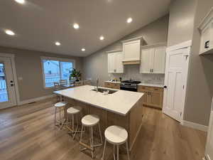 Kitchen featuring vaulted ceiling, recessed lighting, decorative backsplash, light stone counters, and a kitchen island with sink