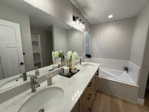 Bathroom with dark wood-type flooring, double vanity, a garden tub, recessed lighting, and a walk in closet