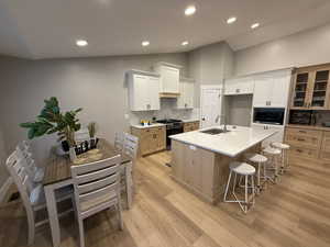 Kitchen with a kitchen bar, glass insert cabinets, decorative backsplash, stainless steel range with gas stovetop, and recessed lighting