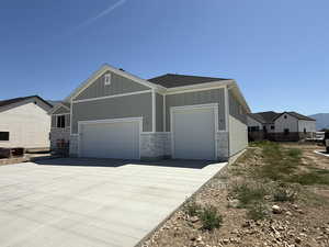 View of front of house with board and batten siding, an attached garage, stone siding, and driveway