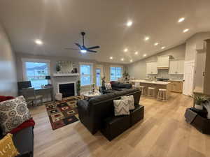 Living room with vaulted ceiling, recessed lighting, light wood finished floors, a fireplace with flush hearth, and a ceiling fan