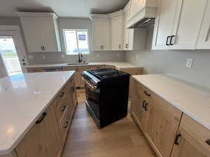 Kitchen featuring light stone counters, black gas range oven, light wood-style floors, custom range hood, and white cabinets