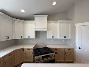 Kitchen with gas stove, lofted ceiling, recessed lighting, light stone countertops, and white cabinetry