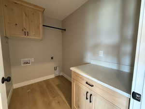 Laundry area with cabinet space, light wood finished floors, washer hookup, and electric dryer hookup