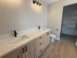 Full bath featuring double vanity, light wood finished floors, and a spacious closet