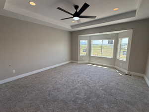 Carpeted spare room featuring a tray ceiling, recessed lighting, and ceiling fan