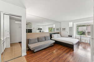 Bedroom featuring freestanding refrigerator, wood finished floors, a closet, and an AC wall unit