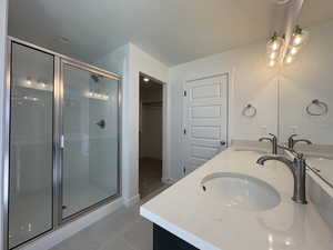 Bathroom featuring double vanity, a spacious closet, a stall shower, a textured ceiling, and light tile patterned floors
