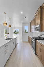 Kitchen with stainless steel appliances, light stone counters, decorative light fixtures, backsplash, and light wood-style floors