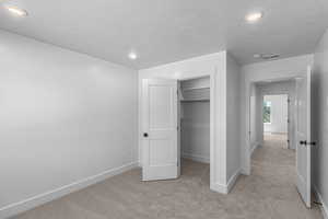 Unfurnished bedroom featuring light carpet, a textured ceiling, recessed lighting, and a walk in closet