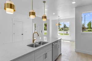 Kitchen featuring light stone countertops, pendant lighting, stainless steel dishwasher, white cabinetry, and light wood-type flooring