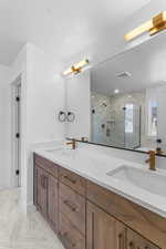 Full bath with light marble finish floors, double vanity, and a marble finish shower