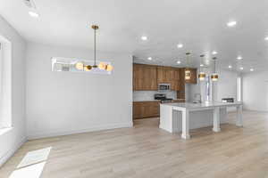 Kitchen with brown cabinets, a center island with sink, pendant lighting, recessed lighting, and a breakfast bar area