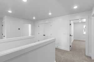 Corridor with an upstairs landing, light carpet, and recessed lighting