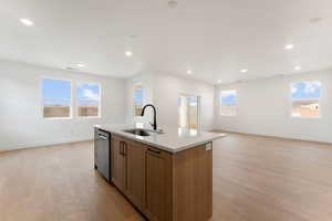Kitchen featuring brown cabinetry, open floor plan, a center island with sink, light wood-style flooring, and recessed lighting