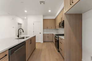 Kitchen featuring appliances with stainless steel finishes, tasteful backsplash, light stone counters, light wood-style flooring, and recessed lighting