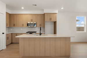 Kitchen with backsplash, appliances with stainless steel finishes, light wood finished floors, an island with sink, and recessed lighting