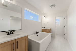 Full bath with two vanities, a freestanding bath, and light tile patterned floors