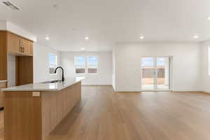 Kitchen featuring light wood finished floors, healthy amount of natural light, recessed lighting, light stone countertops, and a kitchen island with sink