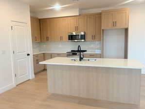 Kitchen with backsplash, light stone countertops, stainless steel appliances, and light brown cabinetry