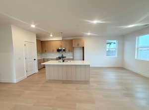 Kitchen featuring decorative backsplash, an island with sink, light wood finished floors, stainless steel appliances, and recessed lighting
