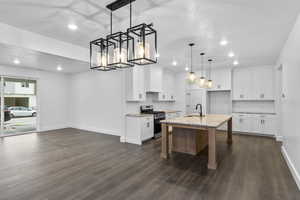 Kitchen featuring white cabinets, gas stove, a center island with sink, pendant lighting, and dark wood-style flooring