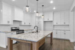 Kitchen with backsplash, white cabinetry, light stone counters, dark wood-type flooring, and recessed lighting