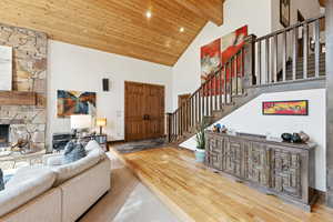 Living area with high vaulted ceiling, wood finished floors, wooden ceiling, stairs, and a stone fireplace