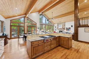 Kitchen with light stone counters, high vaulted ceiling, brown cabinets, light wood-type flooring, and stainless steel gas cooktop