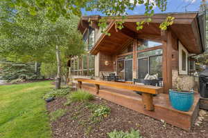 Rear view of property with a deck, a yard, a sunroom, and stone siding