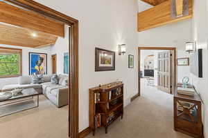 Corridor with light carpet, arched walkways, a wooden ceiling with exposed beams, and high vaulted ceiling