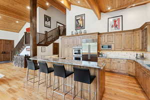 Kitchen with high vaulted ceiling, built in appliances, light stone countertops, a kitchen breakfast bar, and a wooden ceiling with exposed beams