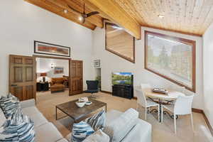 Carpeted living room featuring high vaulted ceiling, a ceiling fan, and a wooden ceiling with exposed beams
